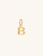 A gold caplital letter B approximately 8mm x 6mm with a connecting ring to thread through a necklace at the top. Set on a cream background.