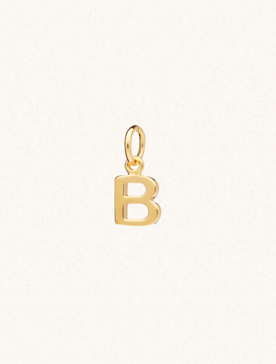 A gold caplital letter B approximately 8mm x 6mm with a connecting ring to thread through a necklace at the top. Set on a cream background.