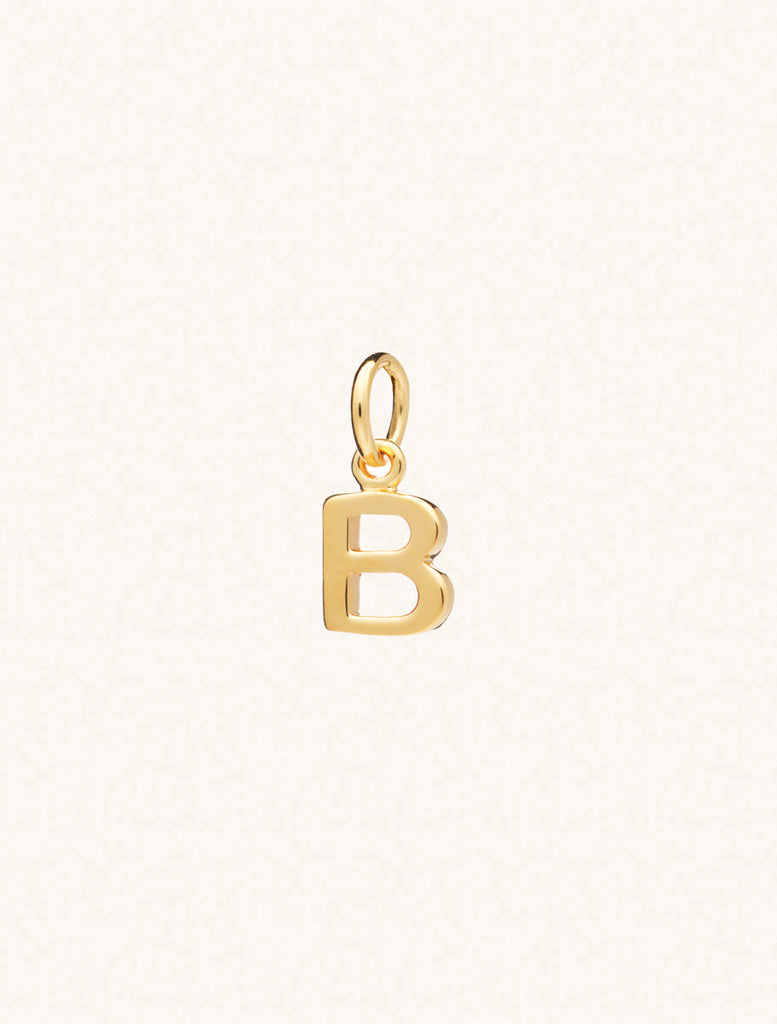 A gold caplital letter B approximately 8mm x 6mm with a connecting ring to thread through a necklace at the top. Set on a cream background.