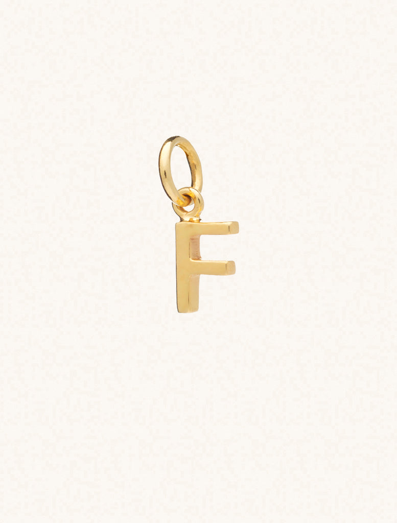 A gold caplital letter F approximately 8mm x 6mm with a connecting ring to thread through a necklace at the top. Set on a cream background.