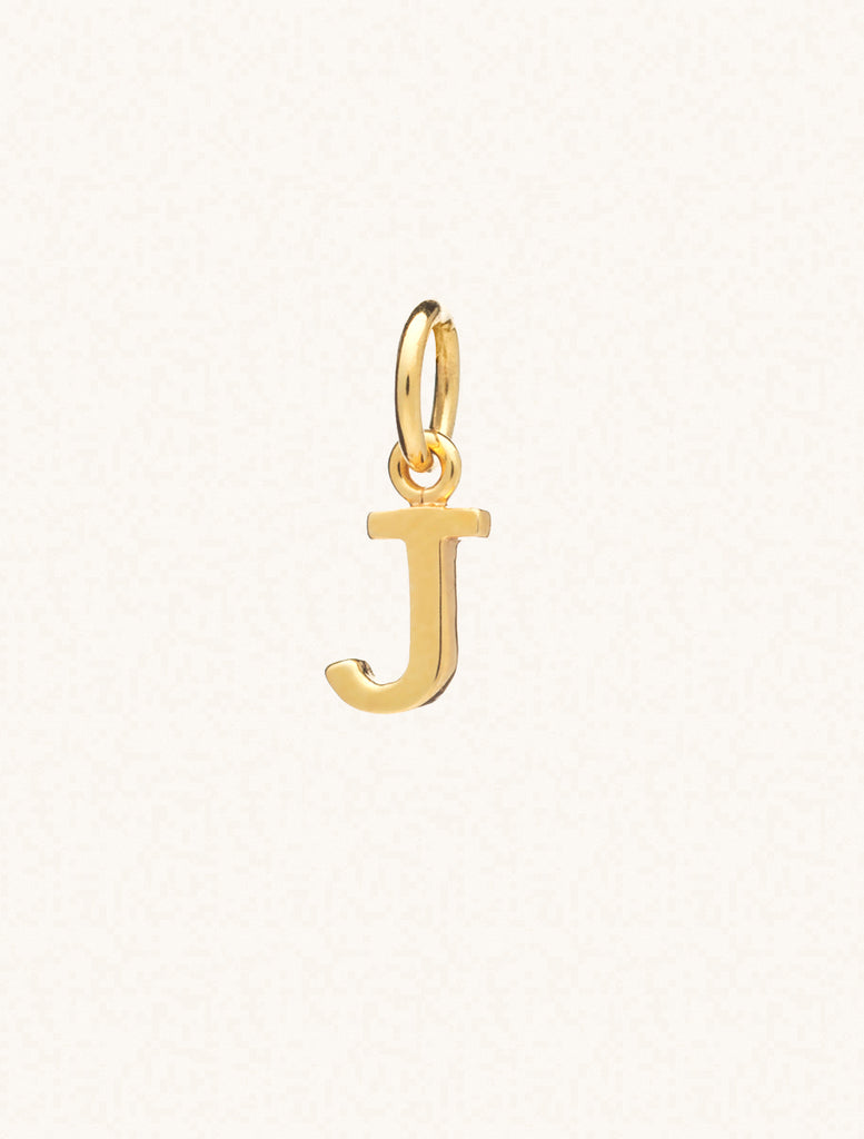 A gold caplital letter J approximately 8mm x 6mm with a connecting ring to thread through a necklace at the top. Set on a cream background.