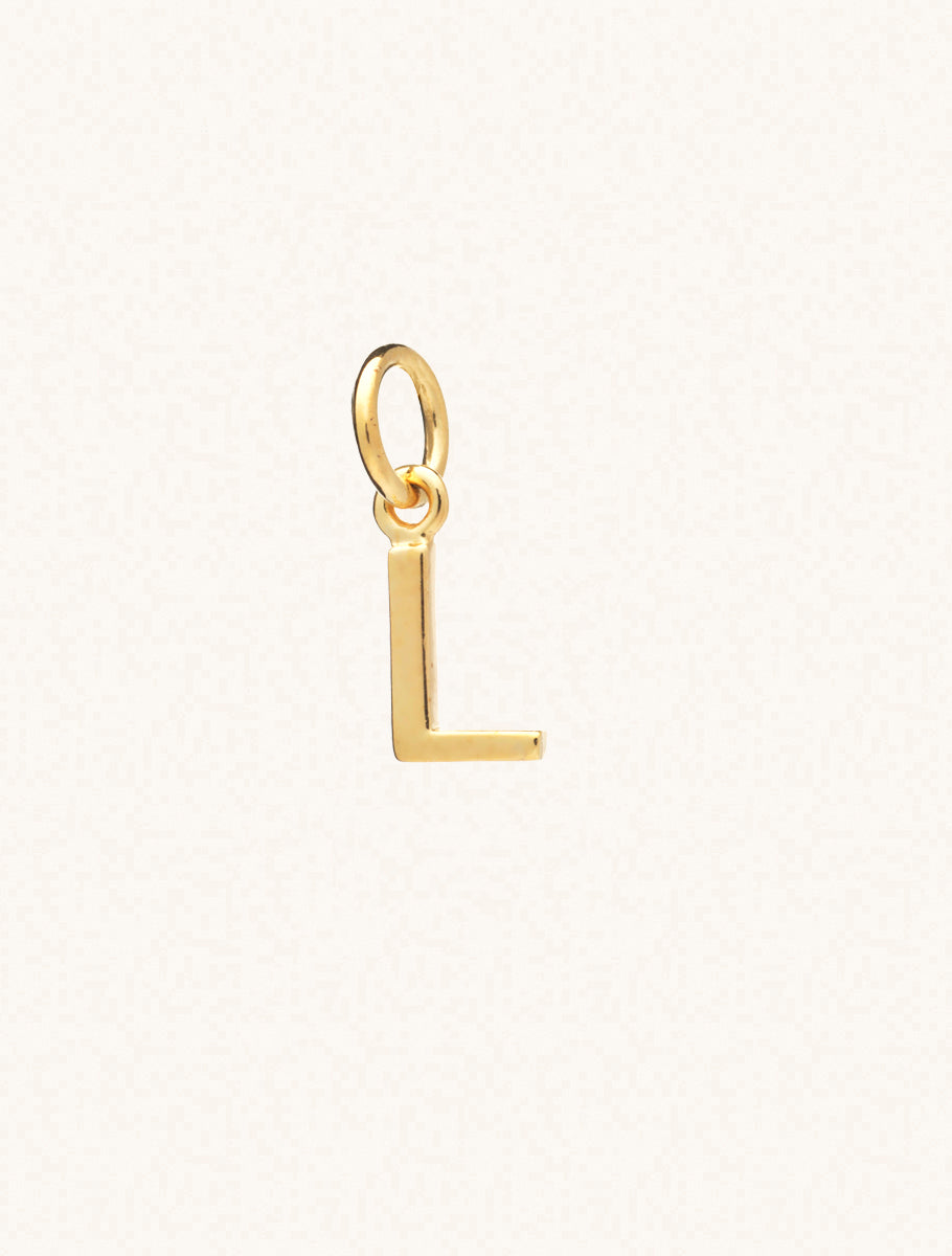 A gold caplital letter L approximately 8mm x 6mm with a connecting ring to thread through a necklace at the top. Set on a cream background.