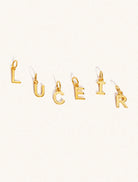 Gold initials approximately 8mm x 6mm in capitals spelling out Luceir. Set on a cream background with gentle shadowing.