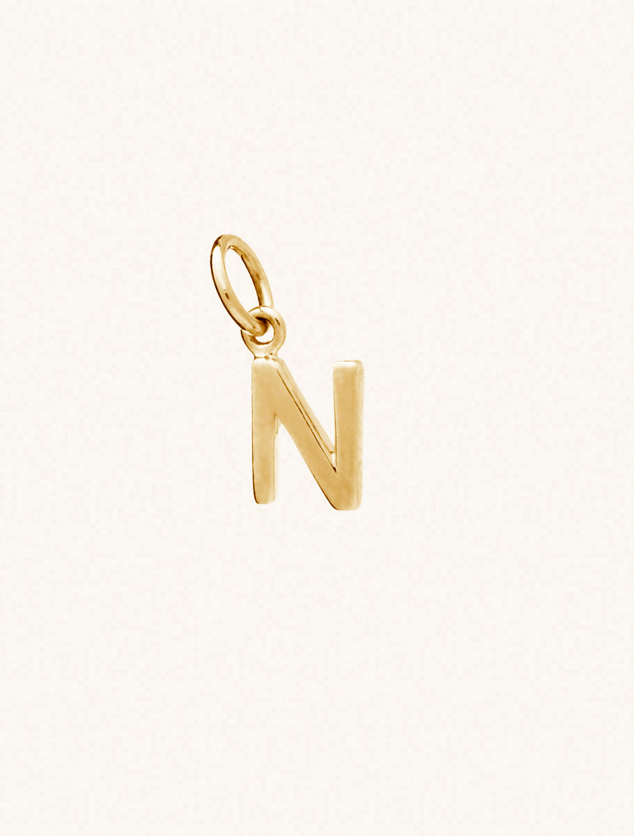 A gold caplital letter N approximately 8mm x 6mm with a connecting ring to thread through a necklace at the top. Set on a cream background.