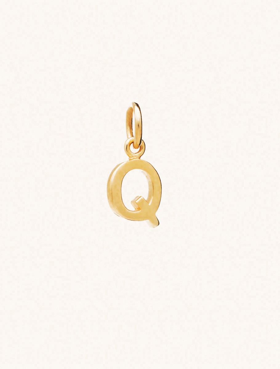 A gold caplital letter Q approximately 8mm x 6mm with a connecting ring to thread through a necklace at the top. Set on a cream background.