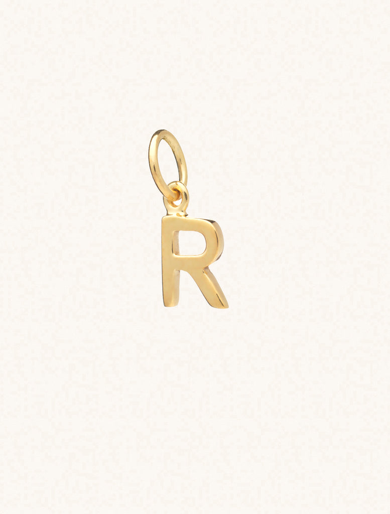 A gold caplital letter R approximately 8mm x 6mm with a connecting ring to thread through a necklace at the top. Set on a cream background.