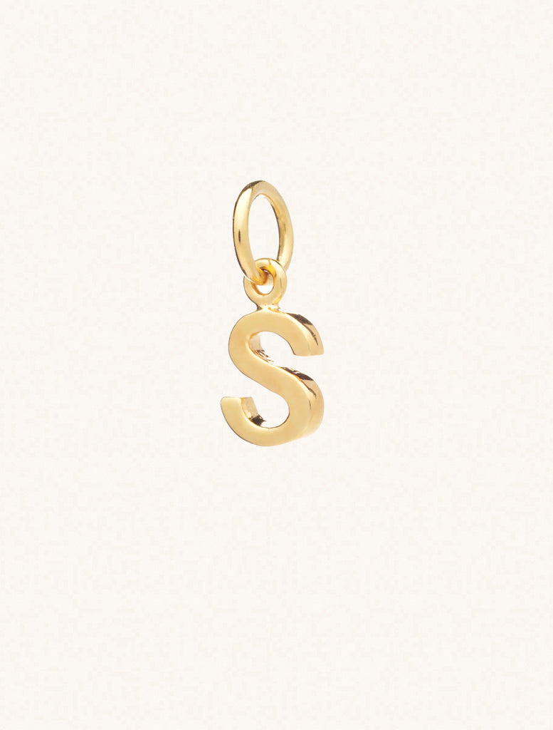 A gold caplital letter S approximately 8mm x 6mm with a connecting ring to thread through a necklace at the top. Set on a cream background.