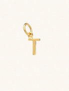 A gold caplital letter T approximately 8mm x 6mm with a connecting ring to thread through a necklace at the top. Set on a cream background.