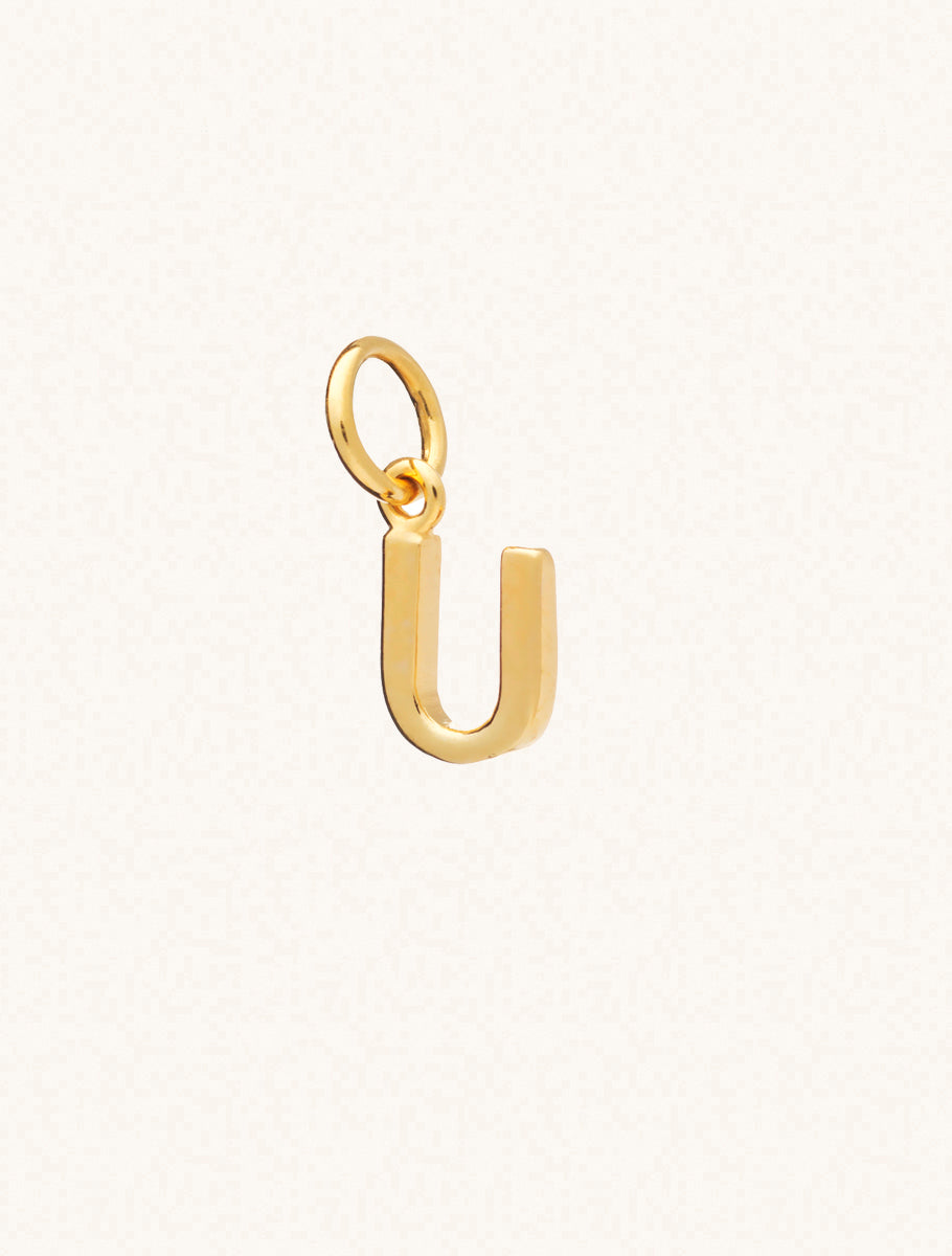 A gold caplital letter U approximately 8mm x 6mm with a connecting ring to thread through a necklace at the top. Set on a cream background.