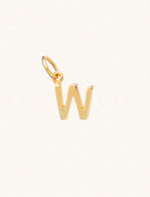 A gold caplital letter W approximately 8mm x 6mm with a connecting ring to thread through a necklace at the top. Set on a cream background.