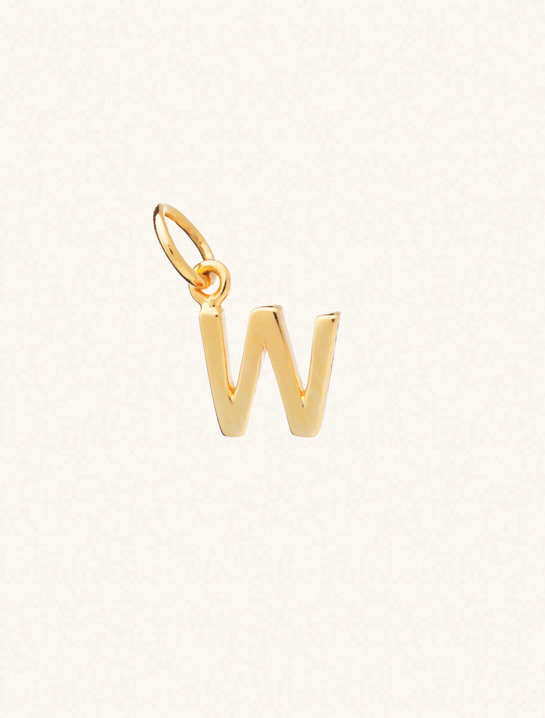 A gold caplital letter W approximately 8mm x 6mm with a connecting ring to thread through a necklace at the top. Set on a cream background.