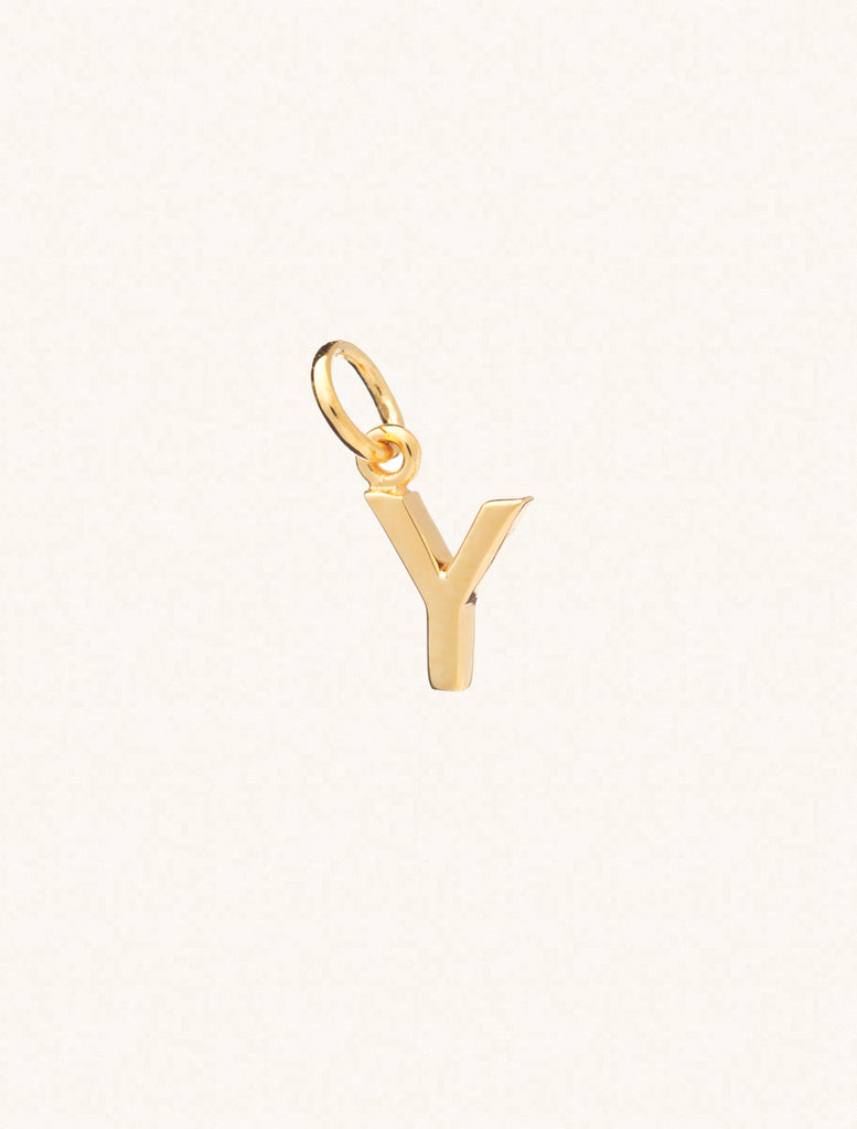 A gold caplital letter Y approximately 8mm x 6mm with a connecting ring to thread through a necklace at the top. Set on a cream background.