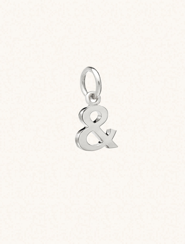 A sterling silver & symbol approximately 8mm x 6mm with a connecting ring to thread through a necklace at the top. Set on a cream background.