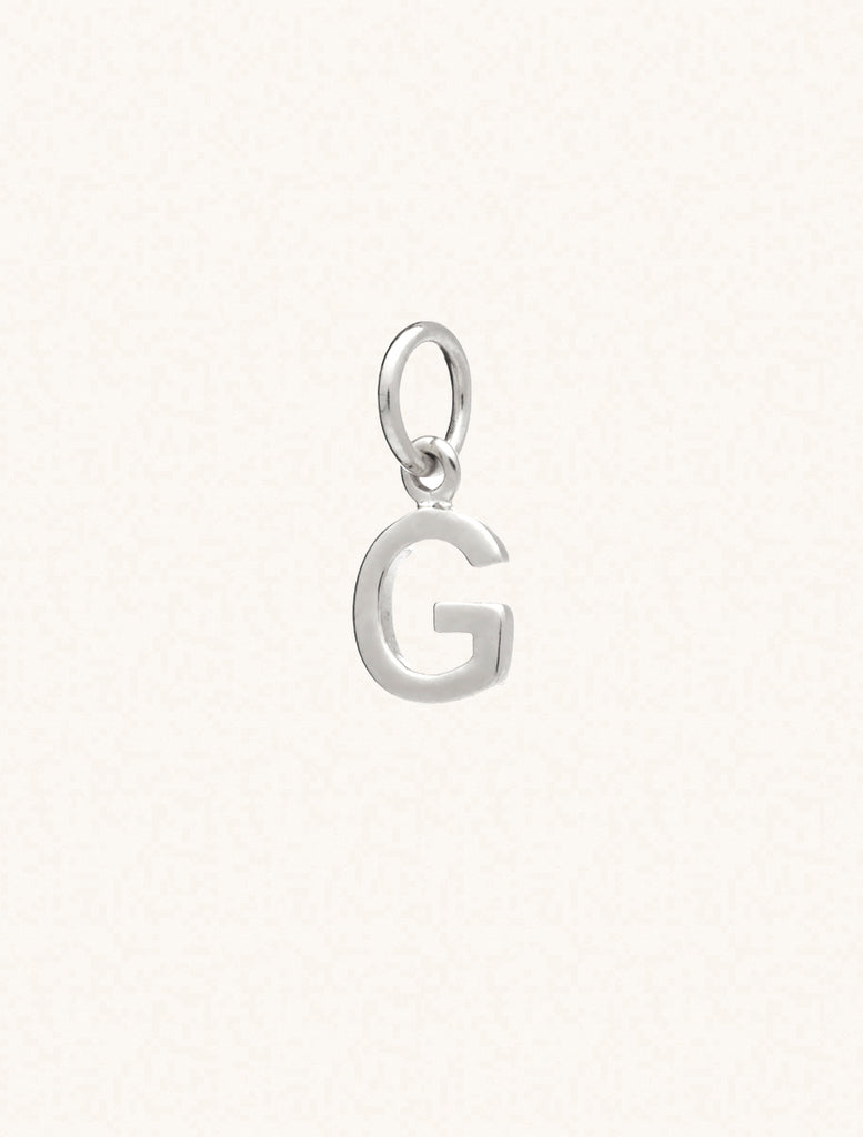 A sterling silver caplital letter G approximately 8mm x 6mm with a connecting ring to thread through a necklace at the top. Set on a cream background.