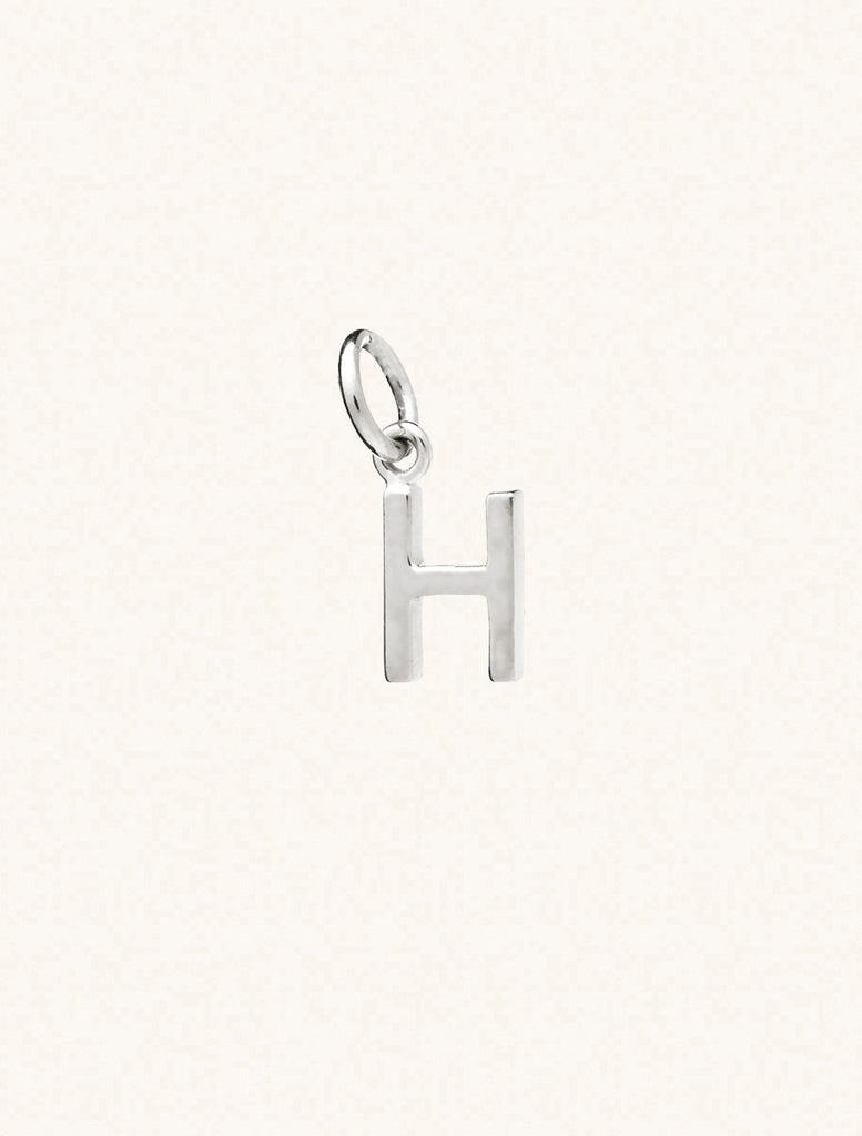 A sterling silver caplital letter H approximately 8mm x 6mm with a connecting ring to thread through a necklace at the top. Set on a cream background.