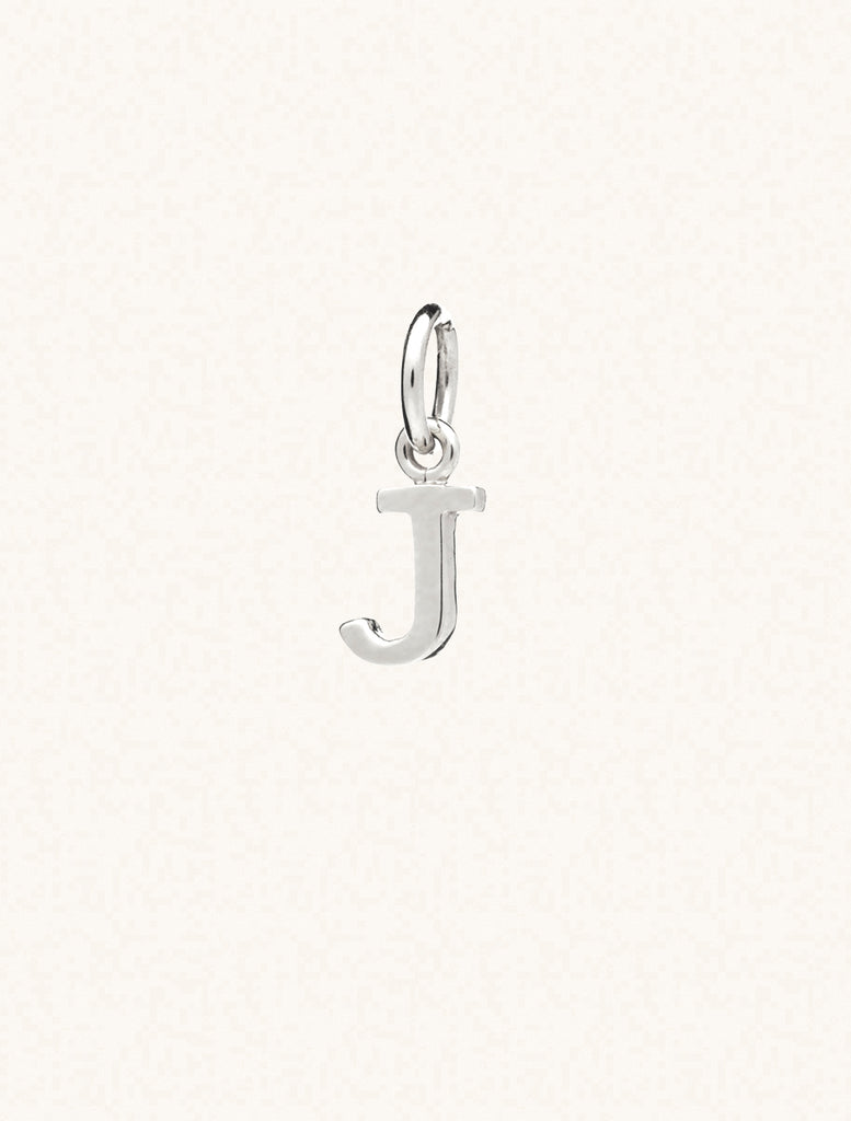 A sterling silver caplital letter J approximately 8mm x 6mm with a connecting ring to thread through a necklace at the top. Set on a cream background.