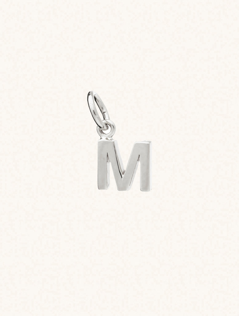 A sterling silver caplital letter M approximately 8mm x 6mm with a connecting ring to thread through a necklace at the top. Set on a cream background.