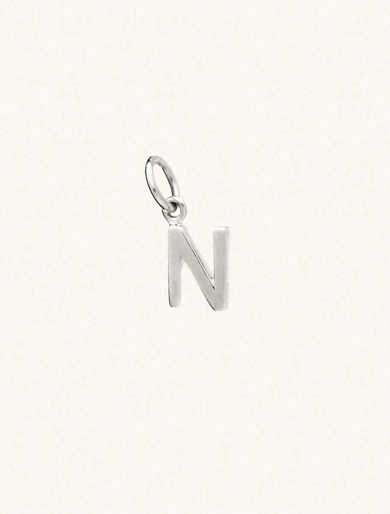 A sterling silver caplital letter N approximately 8mm x 6mm with a connecting ring to thread through a necklace at the top. Set on a cream background.