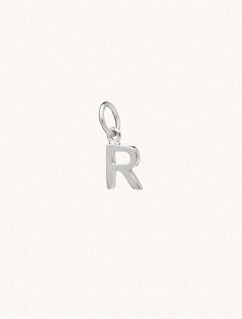 A sterling silver caplital letter R approximately 8mm x 6mm with a connecting ring to thread through a necklace at the top. Set on a cream background.