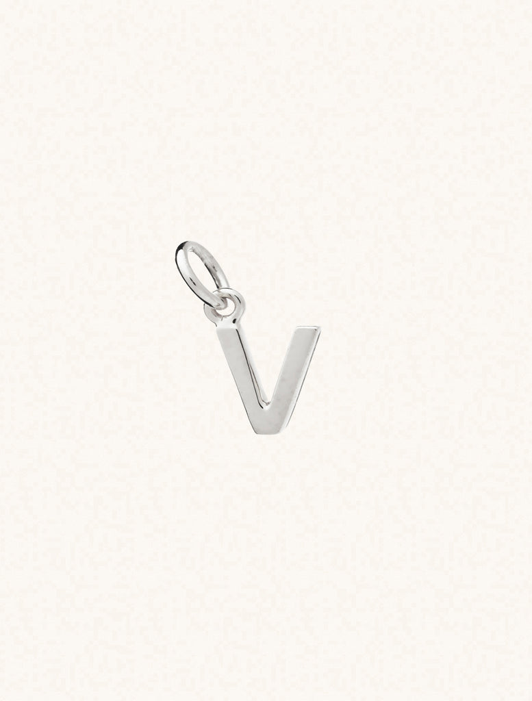 A sterling silver caplital letter V approximately 8mm x 6mm with a connecting ring to thread through a necklace at the top. Set on a cream background.