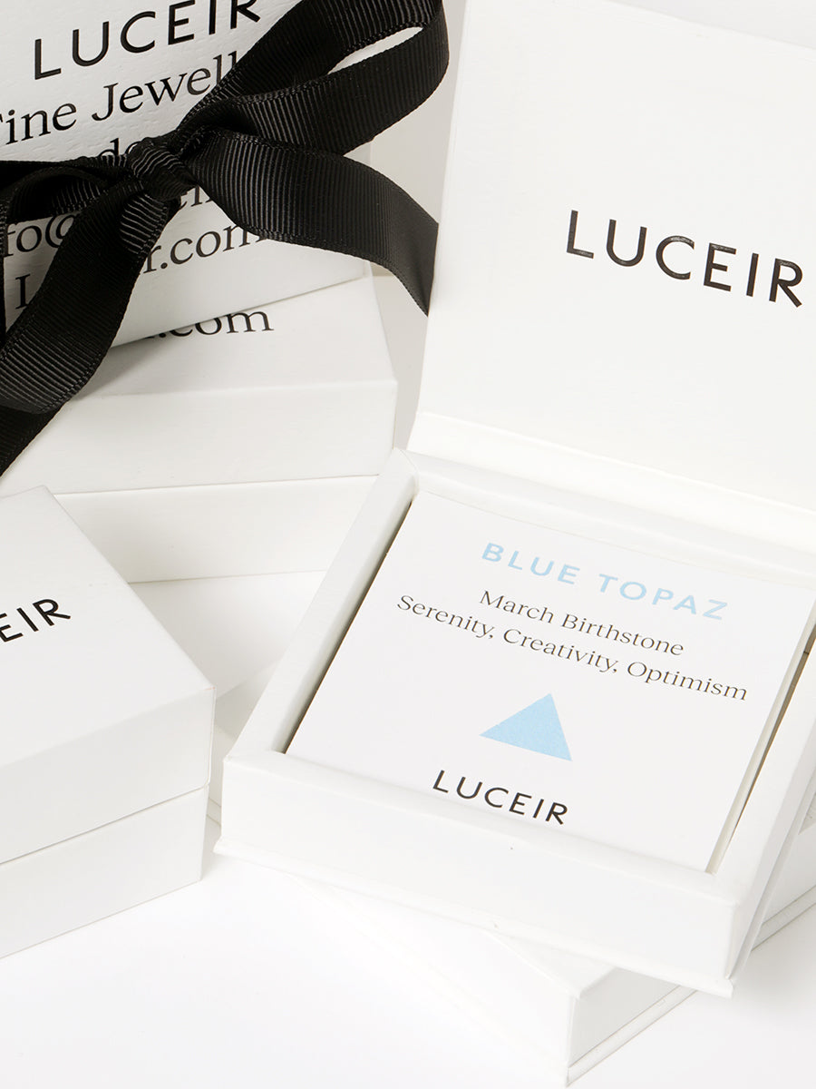 Luceir white packaging card set in a box saying Blue Topaz, March Birthtone, Serenity, Creativity, Optimism followed by a light powder blue triangle symbol underneath with Luceir logo at the bottom